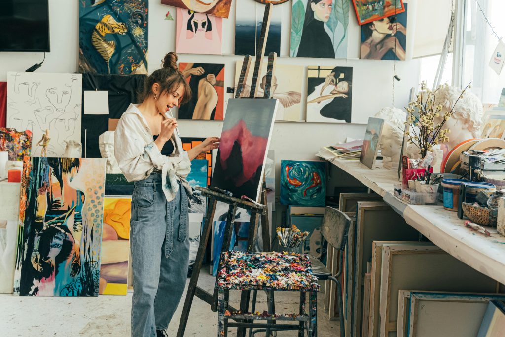 A young woman artist painting on canvas in her vibrant art studio filled with inspiring artworks. Painting techniques for artists. Painting brush types.