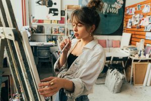 Female artist in a studio, contemplating her next brush stroke on canvas.