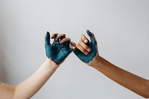 Close-up of two hands with blue paint in a pinky swear gesture, symbolizing connection.